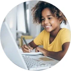 smiling child writing in front of a computer monitor